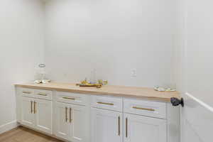 Bar area featuring butcher block counters, white cabinetry, and light wood finished floors