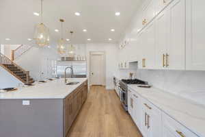 Kitchen with light stone counters, white cabinetry, high quality appliances, pendant lighting, and light wood-type flooring