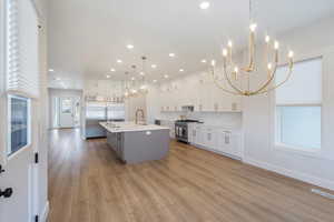 Kitchen featuring a chandelier, white cabinets, high end appliances, a kitchen island with sink, and gray cabinets