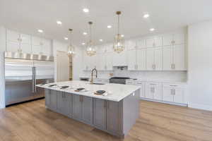 Kitchen featuring white cabinetry, appliances with stainless steel finishes, light stone counters, pendant lighting, and beautful backsplash and counter tops.
