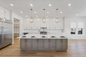 Kitchen with white cabinets, stainless steel appliances, light stone countertops, decorative backsplash, and a large island