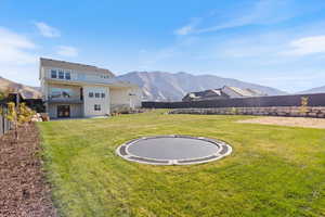 Fenced backyard featuring a trampoline, a mountain view, a balcony, and a patio area