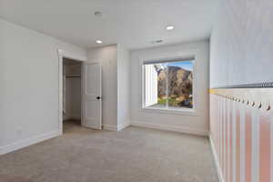 Bedroom with a walk in closet, light colored carpet, and recessed lighting