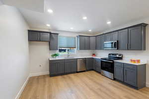 Full kitchen with appliances with stainless steel finishes, light wood-type flooring, recessed lighting, gray cabinetry, and light stone countertops