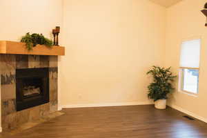 Unfurnished living room featuring dark wood-type flooring and a tile fireplace