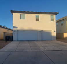 Rear view of property featuring stucco siding, an attached garage, and concrete driveway