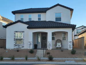 View of front of home featuring a porch, a tiled roof, stucco siding, and stone siding