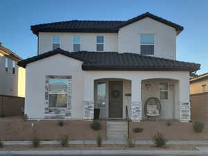 View of front of home featuring a porch, stone siding, a tile roof, and stucco siding