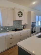 Kitchen with white cabinetry, light wood-style floors, decorative backsplash, appliances with stainless steel finishes, and custom range hood
