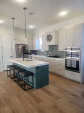 Kitchen featuring decorative backsplash, white cabinets, a center island with sink, and appliances with stainless steel finishes