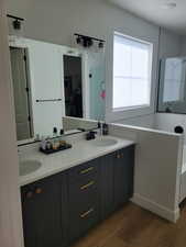 Full bath with a walk in closet, double vanity, dark wood finished floors, a bathtub, and a stall shower