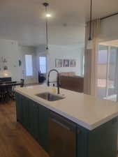 Kitchen featuring open floor plan, dishwasher, dark wood-style floors, decorative light fixtures, and a center island with sink