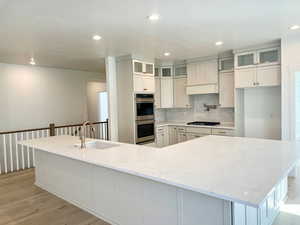 Kitchen featuring decorative backsplash, white cabinets, light stone countertops, recessed lighting, and glass insert cabinets