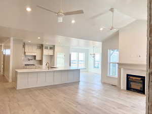 Kitchen featuring a ceiling fan, backsplash, light wood-style floors, white cabinets, and a brick fireplace