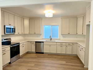 Kitchen featuring appliances with stainless steel finishes, light wood-style floors, a textured ceiling, and white cabinetry