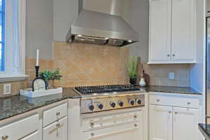 Kitchen with white cabinetry, dark stone countertops, exhaust hood, and tasteful backsplash
