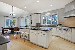 Kitchen featuring wall chimney range hood, tasteful backsplash, white cabinets, pendant lighting, and recessed lighting