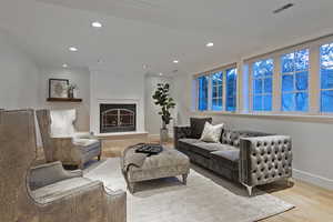 Living room with wood finished floors, recessed lighting, and a lit fireplace