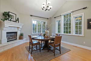 Dining space with light wood-style flooring, vaulted ceiling, a glass covered fireplace, and a chandelier