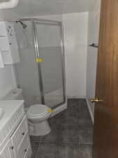 Bathroom featuring dark tile patterned flooring, a shower stall, vanity, and a textured ceiling