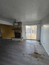 Unfurnished living room with hardwood / wood-style floors, a fireplace, a textured ceiling, and ceiling fan