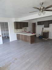 Kitchen with dark brown cabinetry, light countertops, a peninsula, dark wood finished floors, and a textured ceiling