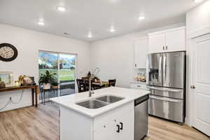 Kitchen featuring stainless steel appliances, white cabinetry, black hardware, light wood finished floors, recessed lighting, and a kitchen island with sink