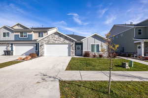 View of front of house featuring board and batten siding, driveway, a 2 car garage, a front lawn, and stone siding