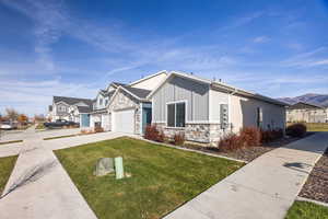 View of front of property featuring stone siding, driveway, a front lawn, and board and batten siding and a 2 car garage