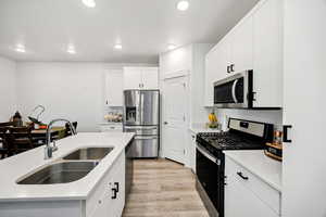 Kitchen featuring appliances with stainless steel finishes,black hardware, light wood finished floors, white cabinets, recessed lighting, and an island with sink