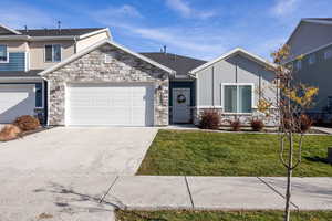 View of front of home featuring stone siding, a front yard, concrete driveway, and an attached 2 car garage