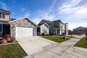 View of front of property featuring a front yard, concrete driveway, stone siding, a 2 car garage, and board and batten siding
