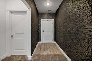 wallpapered Corridor with a textured ceiling and light wood-style flooring