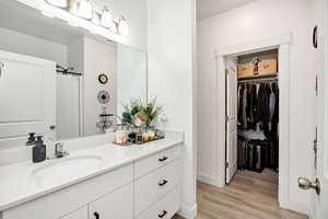 primary Bathroom featuring vanity, a shower with shower curtain, a spacious walk in closet, and light wood-style flooring