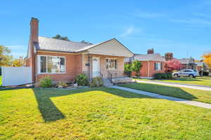View of front of house with a front yard, brick siding, a porch, and a chimney