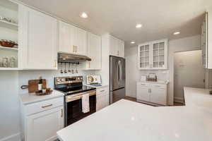 Kitchen with white cabinets, open shelves, stainless steel appliances, glass insert cabinets, and under cabinet range hood