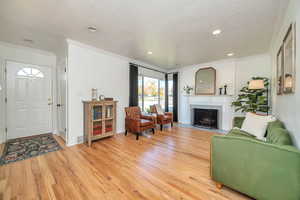 Living area featuring crown molding, light wood finished floors, a fireplace with flush hearth, recessed lighting, and a textured ceiling