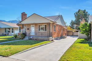 Bungalow featuring a front yard, a porch, a chimney, concrete driveway, and a mountain view