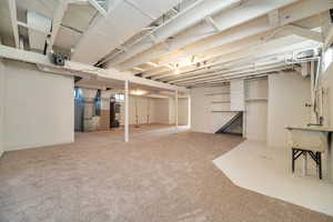 Unfinished below grade area featuring carpet flooring, heating unit, and gas water heater