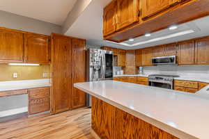 Kitchen with brown cabinets, light wood-type flooring, recessed lighting, appliances with stainless steel finishes, and a peninsula