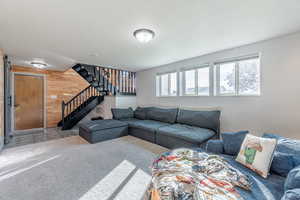 Living room with wood walls, carpet flooring, stairway, and a textured ceiling