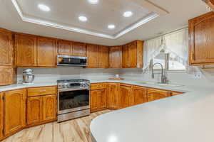 Kitchen featuring a tray ceiling, recessed lighting, brown cabinetry, stainless steel appliances, and light wood-type flooring