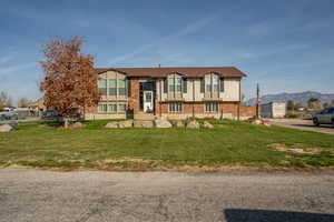 Raised ranch with brick siding, a front lawn, and a mountain view