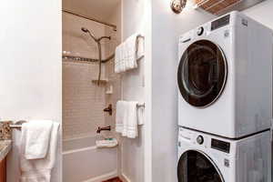 Bathroom featuring a textured wall, bathing tub / shower combination, estacked washer and dryer, vanity, and wood finished floors