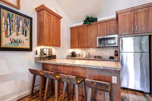 Kitchen with stainless steel appliances, decorative backsplash, light stone countertops, brown cabinets, and a breakfast bar area
