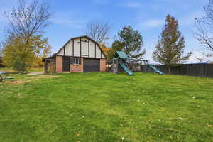Rear view of property with brick siding, a playground, an outbuilding, and a lawn