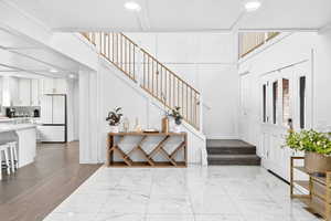 Entrance foyer with recessed lighting, stairs, light marble finish floors, and a towering ceiling