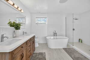 Bathroom with double vanity, a freestanding tub, walk in shower, and light wood-style floors