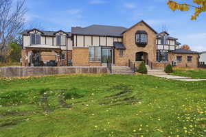 Tudor house with brick siding, a gazebo, a front lawn, stucco siding, and a patio area
