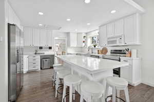 Kitchen featuring white cabinets, recessed lighting, stainless steel appliances, dark wood-type flooring, and a kitchen bar